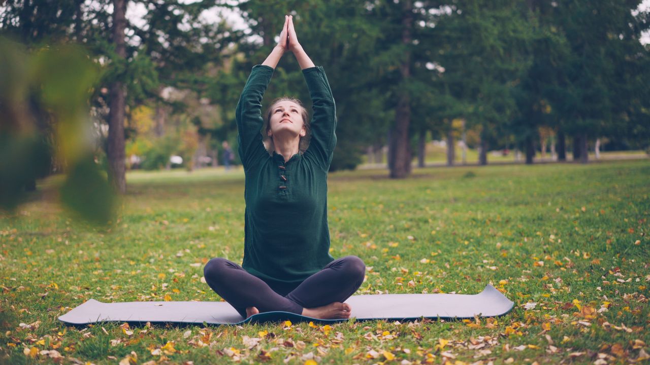 our-story Adult woman practicing yoga in a serene park setting during fall