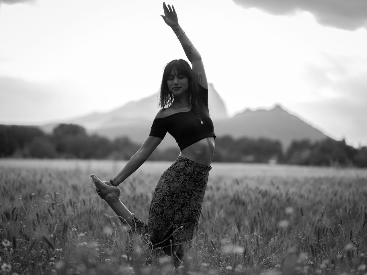 Services-02 Black and white of glad woman in long skirt with raised hand meditating in meadow in daytime